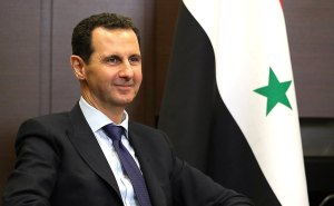Il presidente della Siria Bashar al-Assad in posa con accanto la bandiera del suo Paese